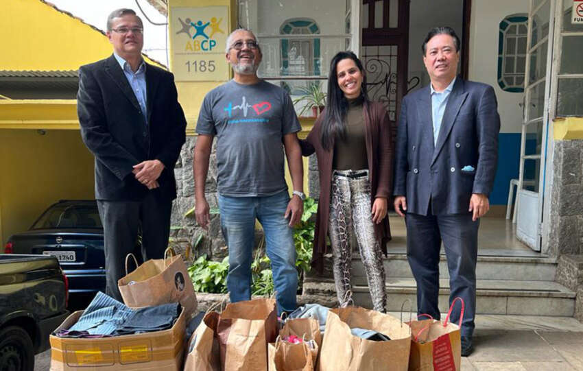 Quatro pessoas, entre elas Paulo Oshiro diretor da DS/SP, em frente a ONG ABCP Associação Beneficente e Comunitária do Povo com sacos de roupas para doação