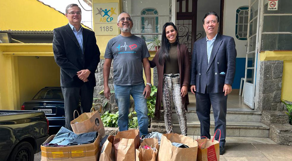 Quatro pessoas, entre elas Paulo Oshiro diretor da DS/SP, em frente a ONG ABCP Associação Beneficente e Comunitária do Povo com sacos de roupas para doação